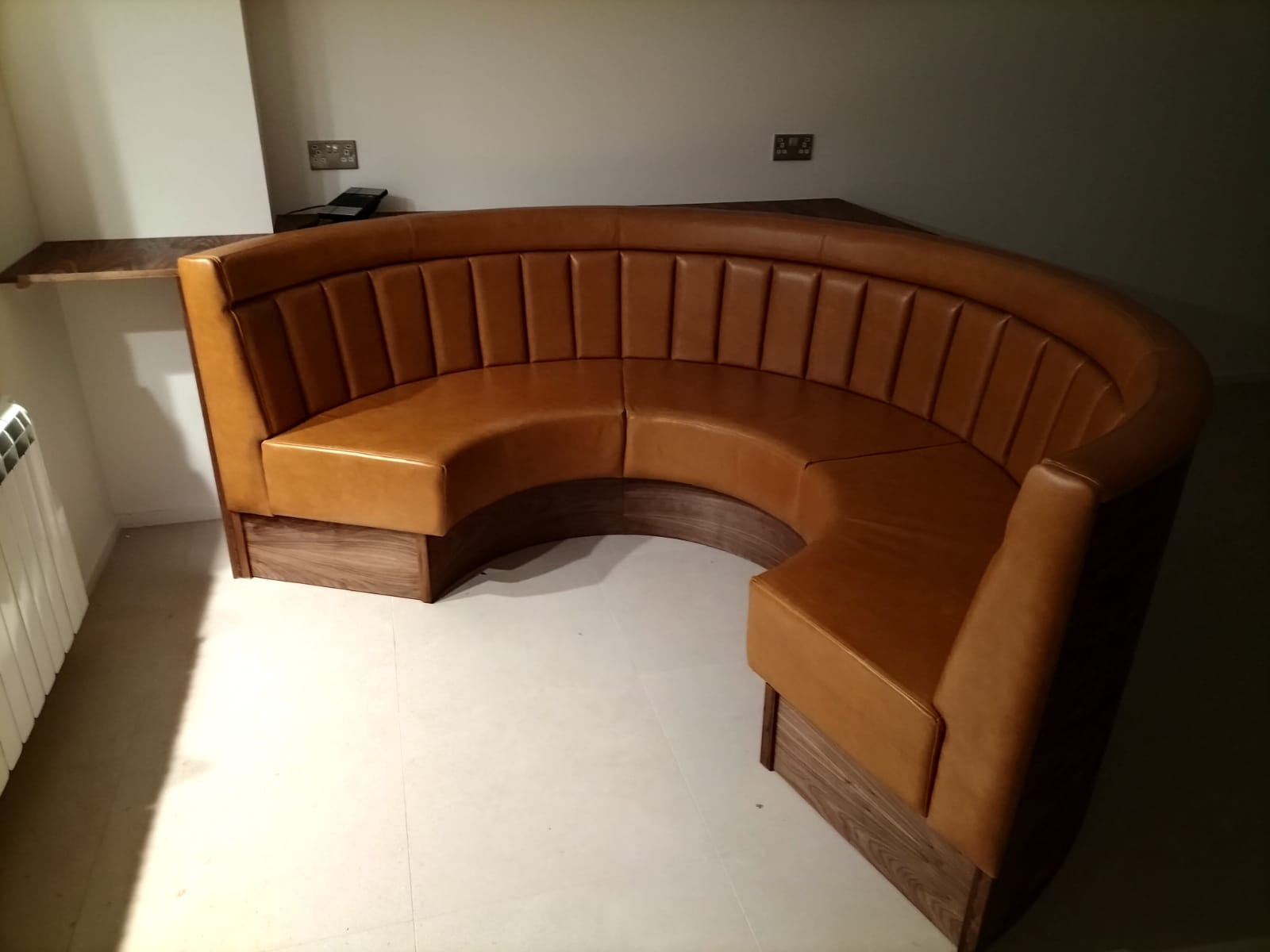 Horseshoe booth in tan leather with fluted backrests, built into a walnut plinth and shelf for a private meeting nook.