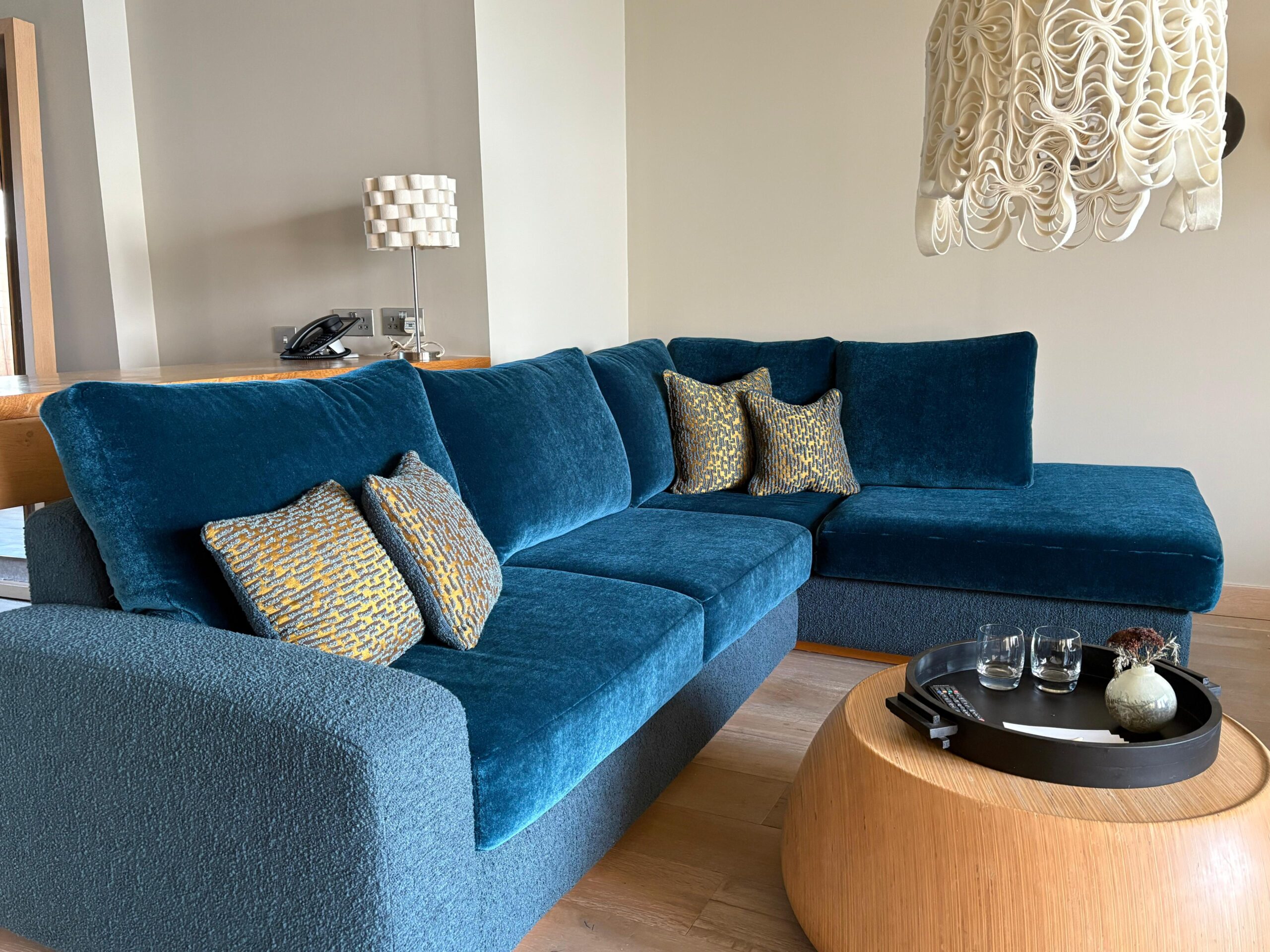 Made-to-measure corner sofa combining teal velvet cushions with a textured boucle base, finished with patterned scatter cushions.
