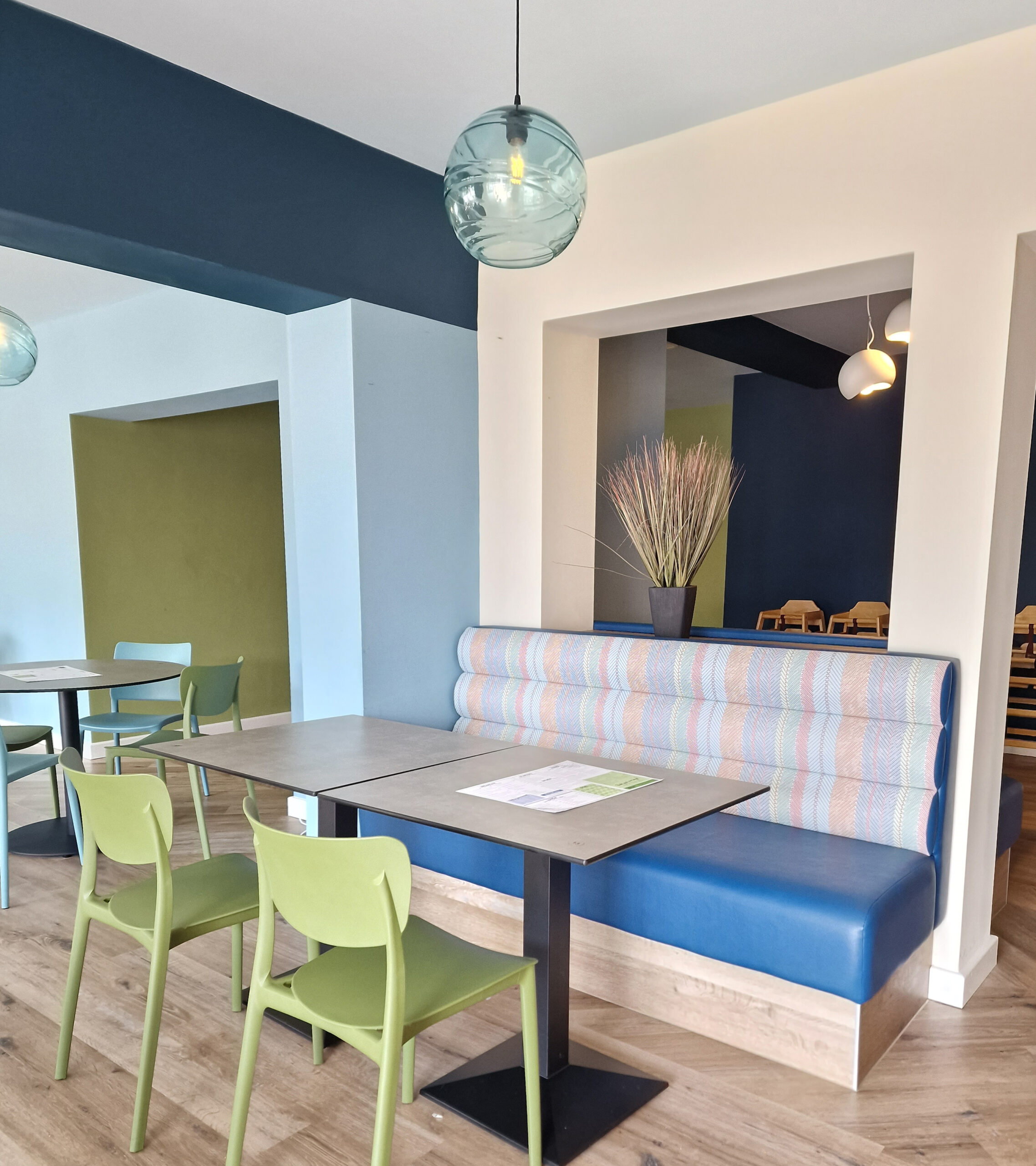 High-back banquette with a pastel herringbone stripe backrest and deep blue leather seat, set on a light oak plinth for a bright terrace dining room.