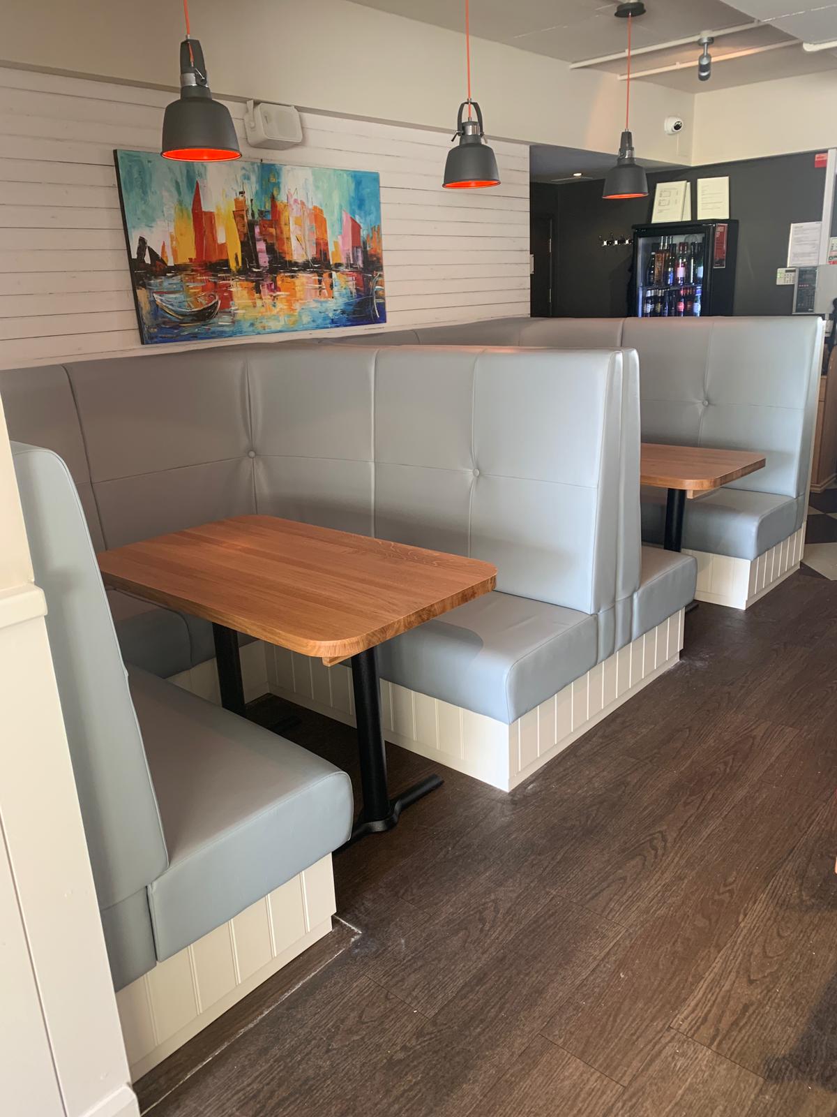 Back-to-back grey leather booths with single-button backs on painted tongue-and-groove plinths, set with solid oak tables.