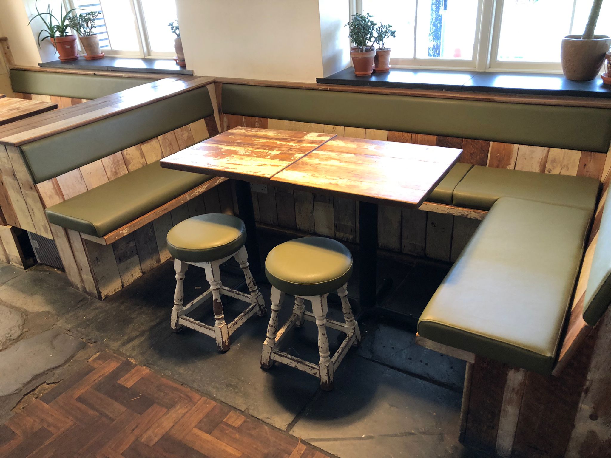 Run of olive green leather benches and matching stools built into reclaimed timber panelling in a village pub.